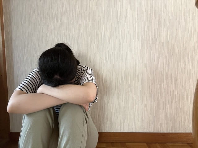 家の壁に座って背をつけて悩む女性